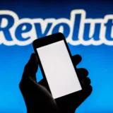 Mână care ține un telefon mobil în fața siglei unei bănci digitale